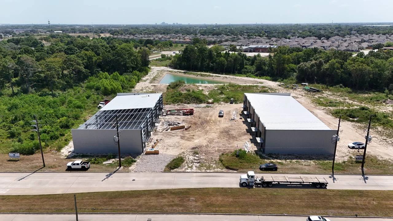Day 176 aerial progress view showing one metal building largely enclosed while roof framing and exterior-envelope installation continue on the adjacent building